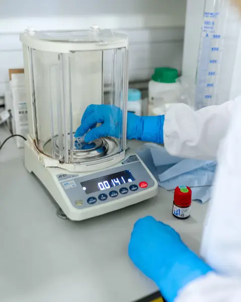 Gloved hands weighing a sample on an analytical balance